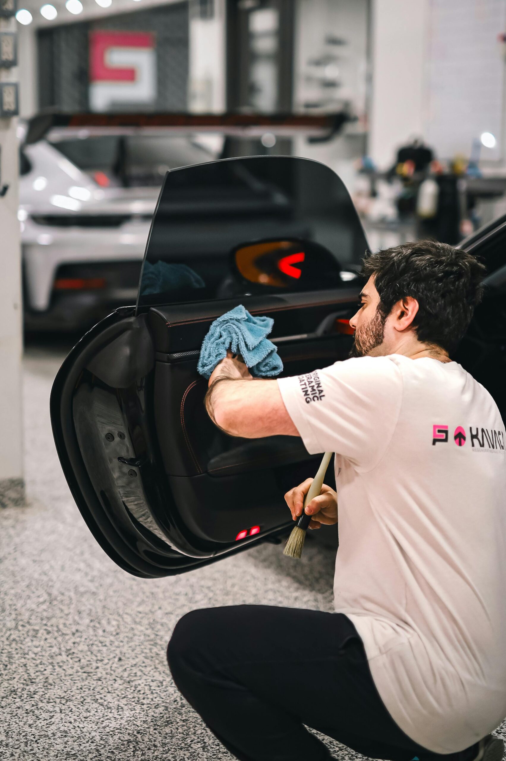 Best Car Vacuums — Proven Way to Keep Your Car Spotless A man meticulously cleans a car door at an auto shop, emphasizing detailing and service.