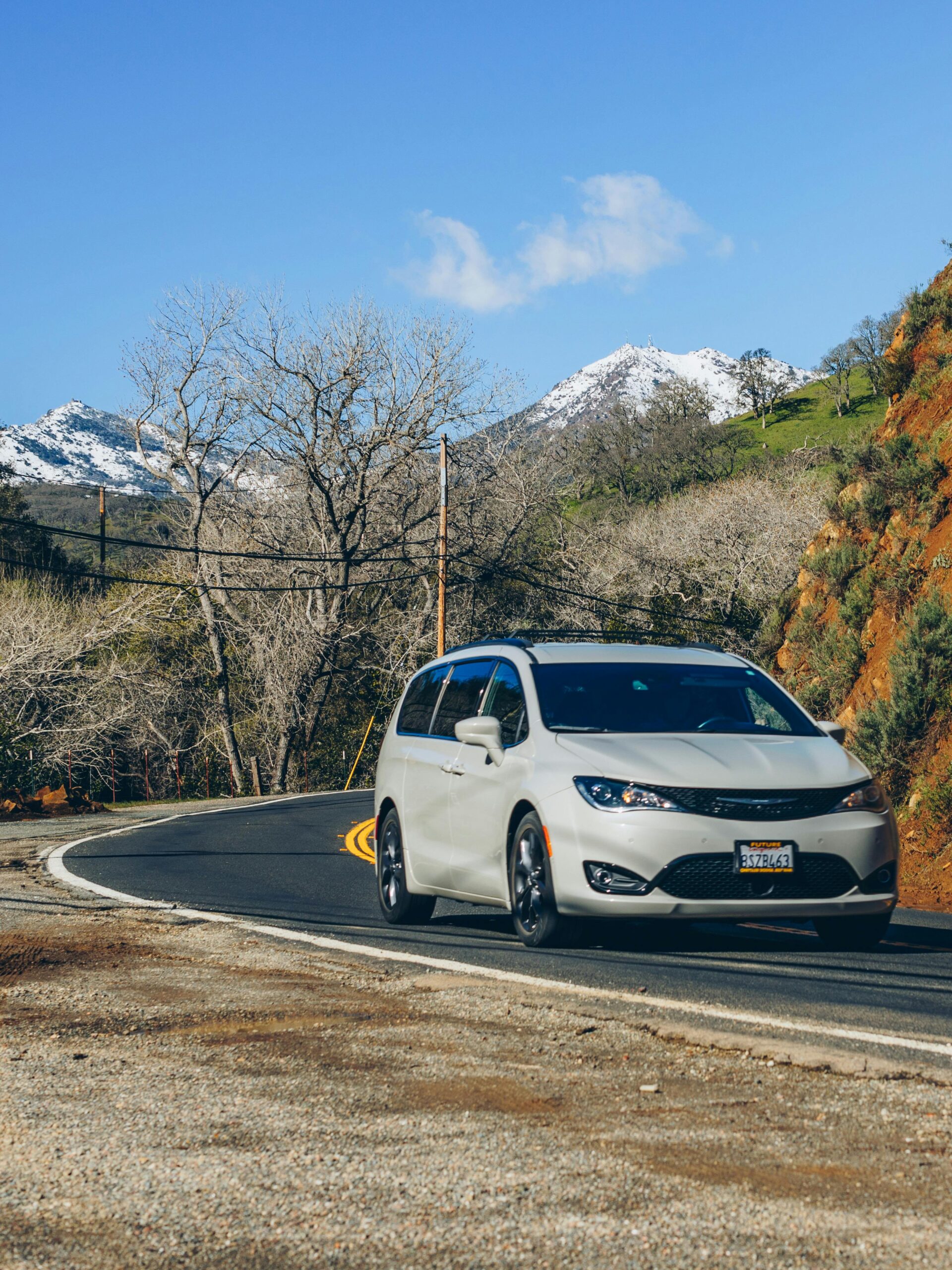 How to Get 250,000 Miles Out of Your Vehicle Minivan driving along a winding mountain road with snowcapped peaks.