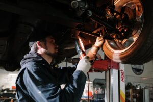 How to Get 250,000 Miles Out of Any Car Mechanic examining car's undercarriage at a garage, focusing on vehicle maintenance.