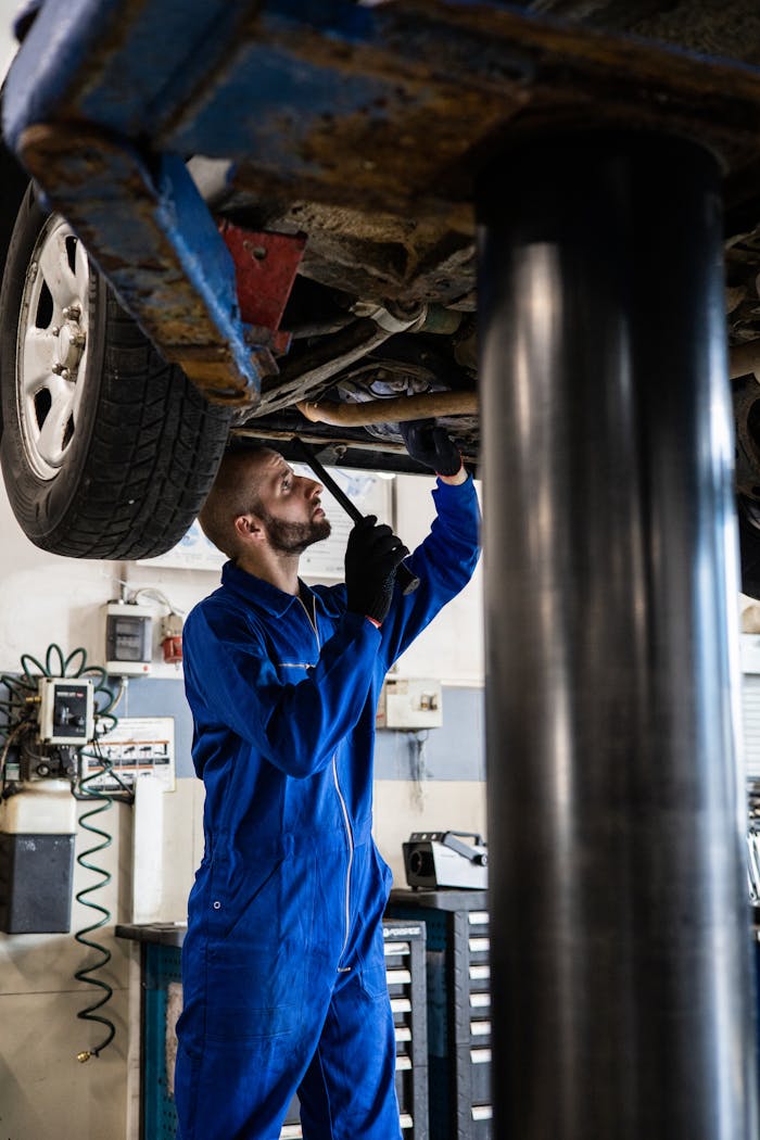 our-experience Mechanic in blue coveralls inspecting car undercarriage on hydraulic lift.